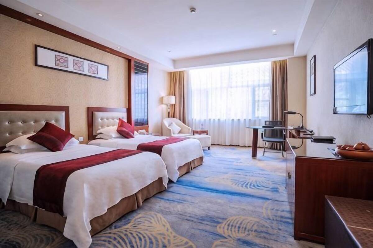 Een hotelkamer met twee bedden, een bureau, een stoel, een televisie en een groot raam.