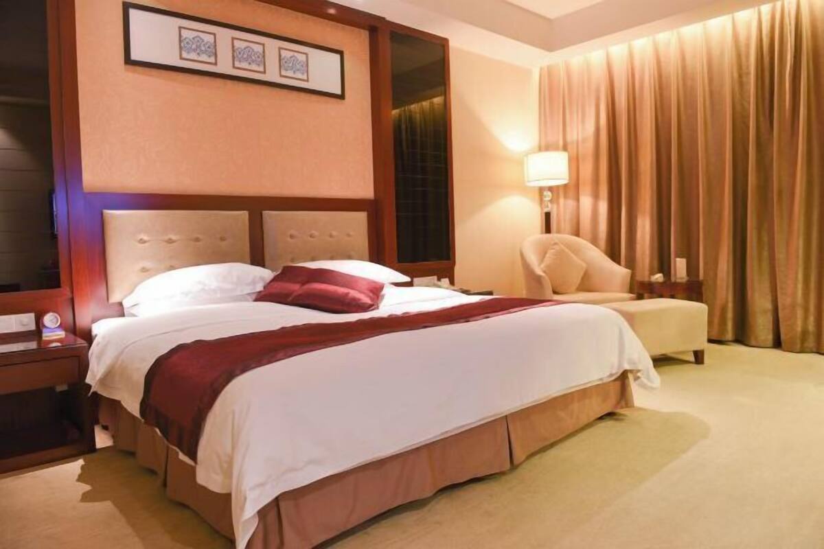 Een hotelkamer met een groot bed, een stoel, een nachtkastje en een lamp.