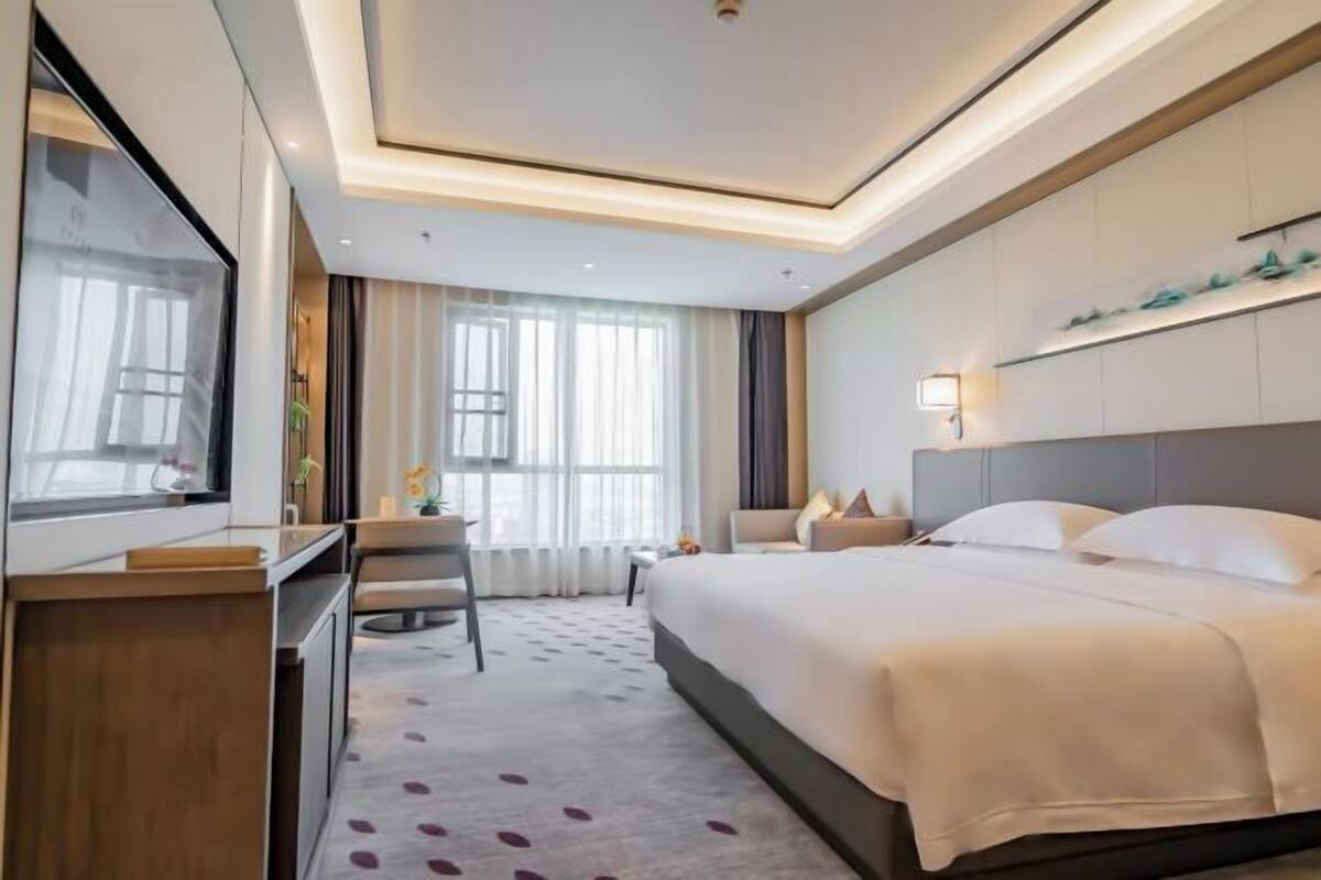 Een moderne hotelkamer met een groot bed, een bureau, een televisie en een raam met gordijnen.