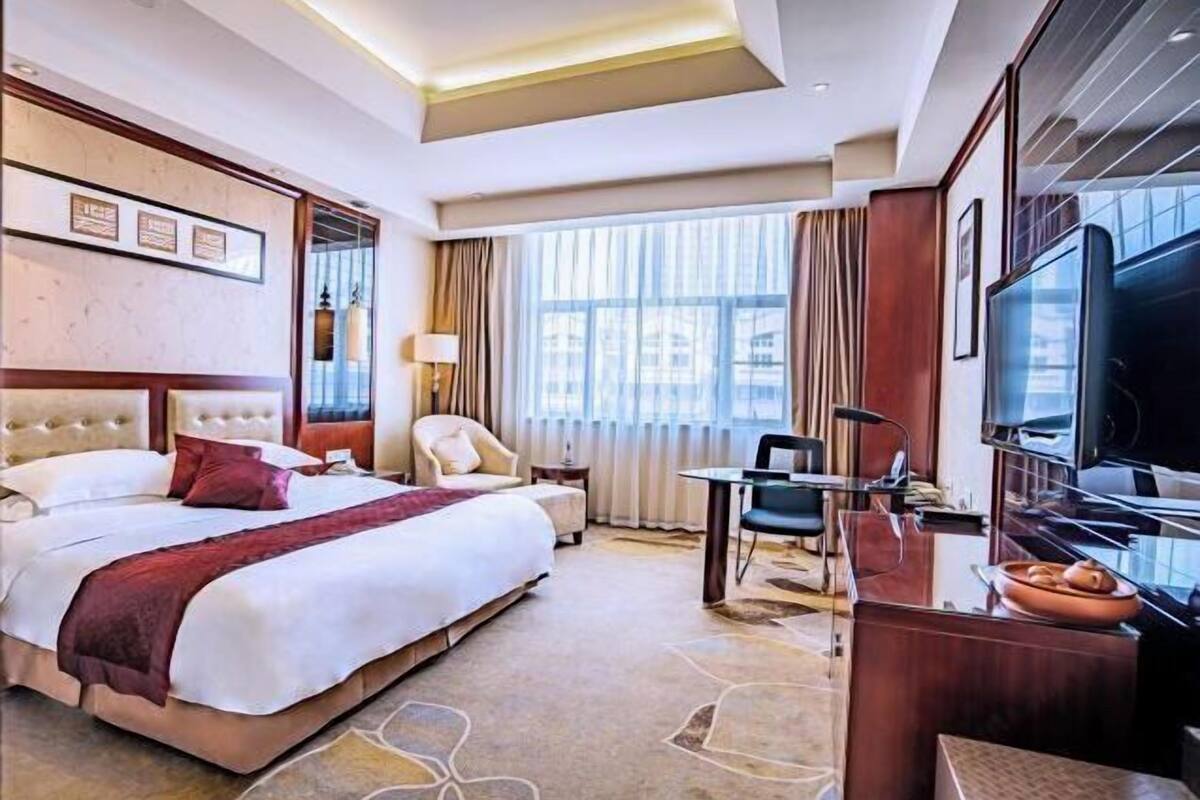Een hotelkamer met een groot bed, een bureau, een stoel, een televisie en een raam met gordijnen.