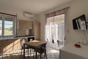 Eine moderne Küche mit Essbereich, ausgestattet mit einem Holztisch und -stühlen, einem eingebauten Ofen und einem großen Fenster mit durchsichtigen Vorhängen.