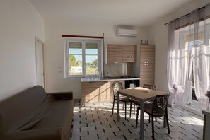 Una cocina compacta con comedor, un sofá y una ventana con cortinas translúcidas.