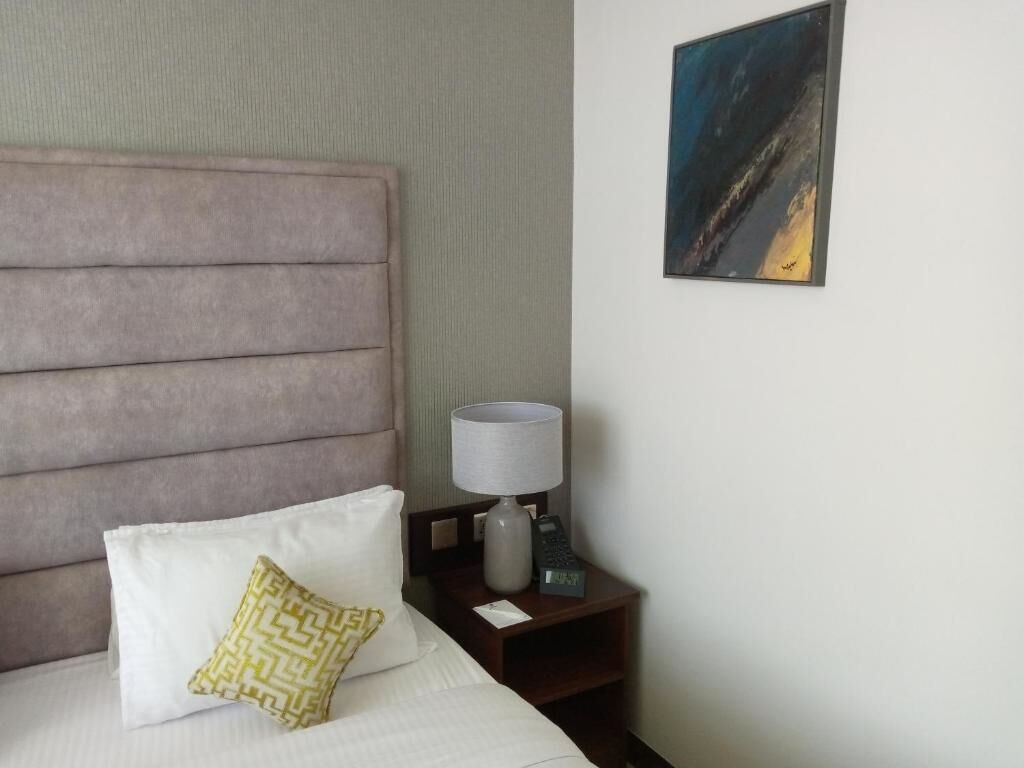 A hotel room with a large bed, a nightstand with a lamp, and a painting on the wall.
