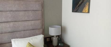 A hotel room with a large bed, a nightstand with a lamp, and a painting on the wall.