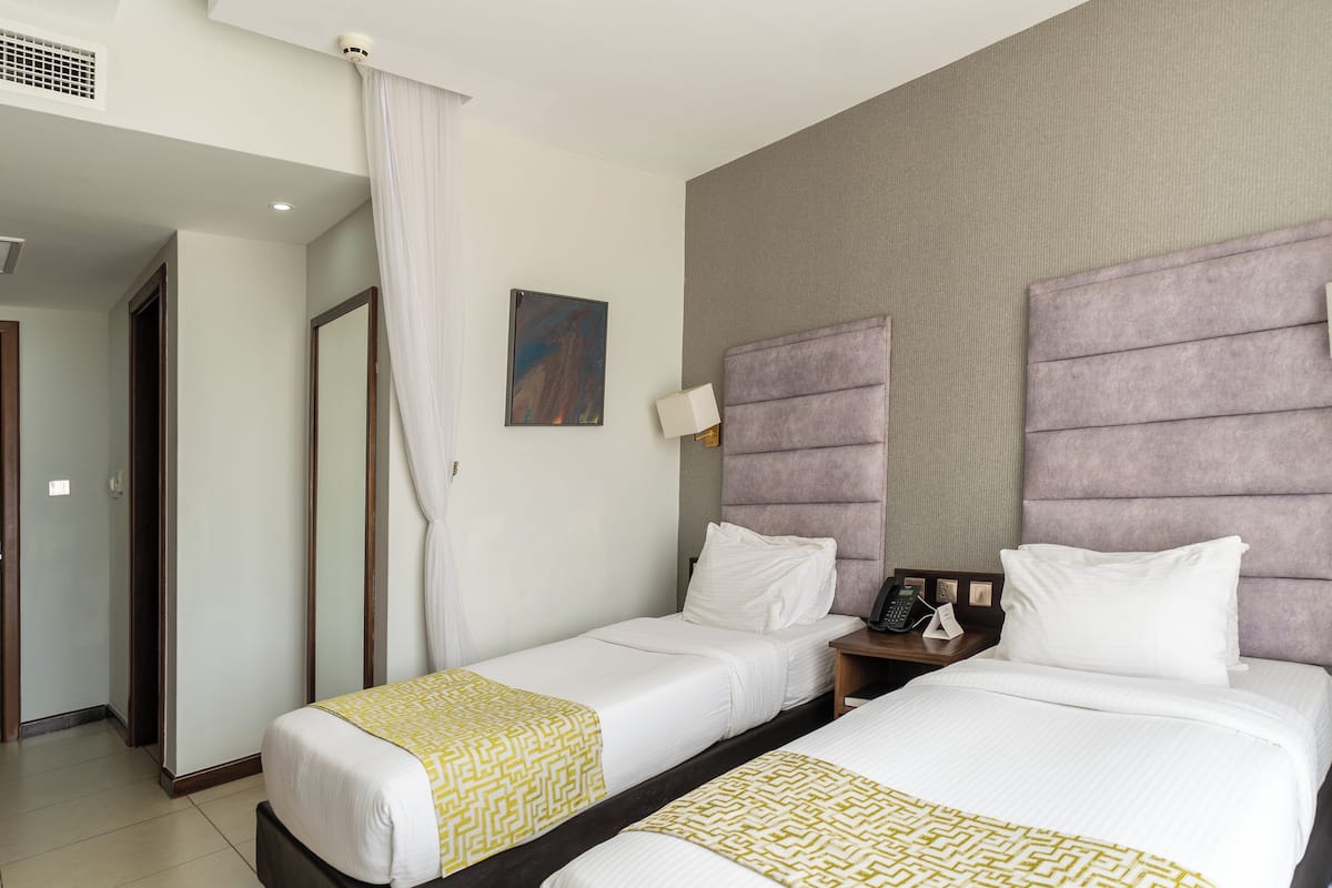 Une chambre d’hôtel avec deux lits, une salle de bain et un petit bureau équipé d’un téléphone et d’une lampe.