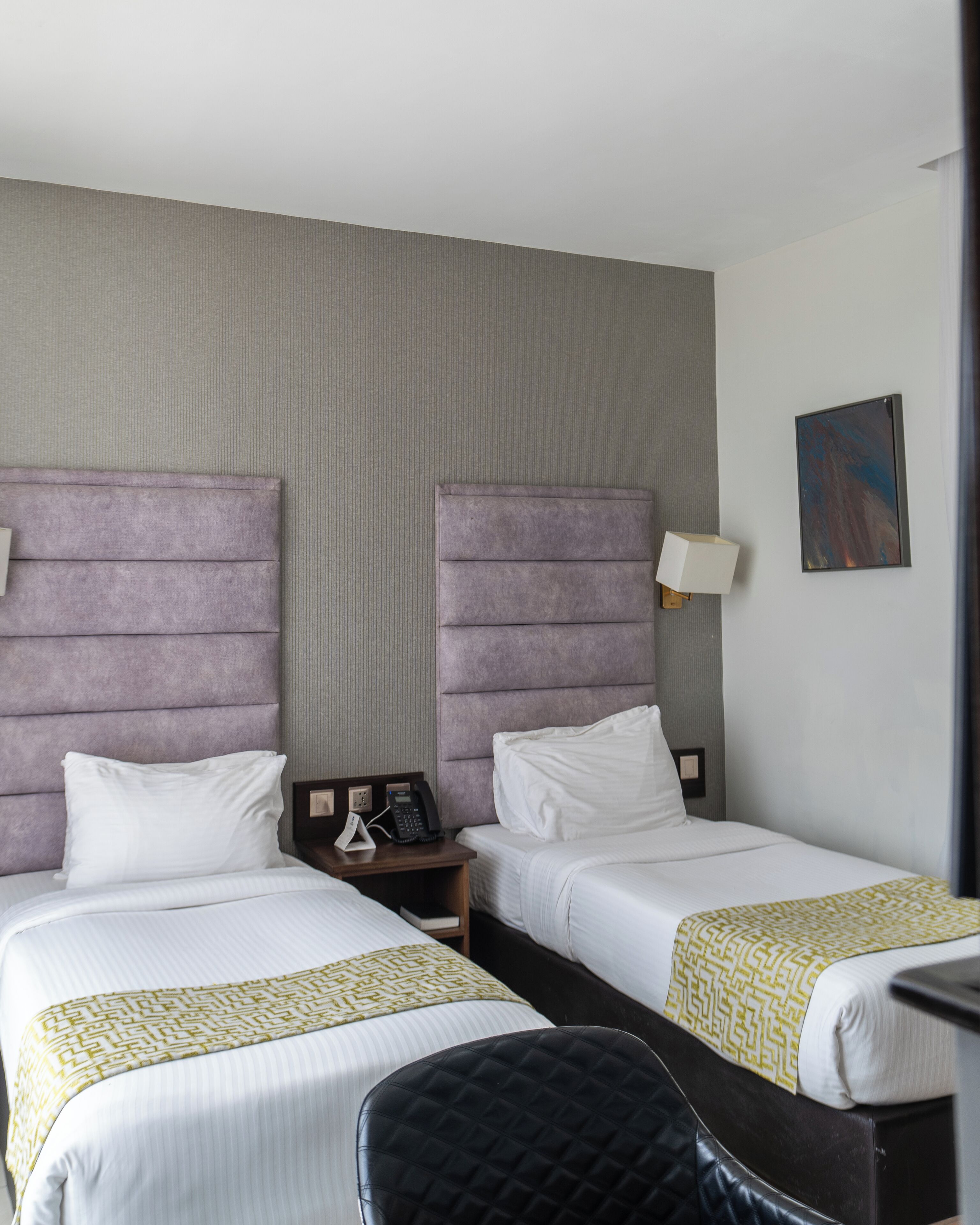 A hotel room with two beds, a nightstand with a phone, a lamp, and a painting on the wall.
