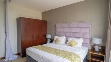 A hotel room with a large bed, a wardrobe, two bedside tables with lamps, and a curtain.