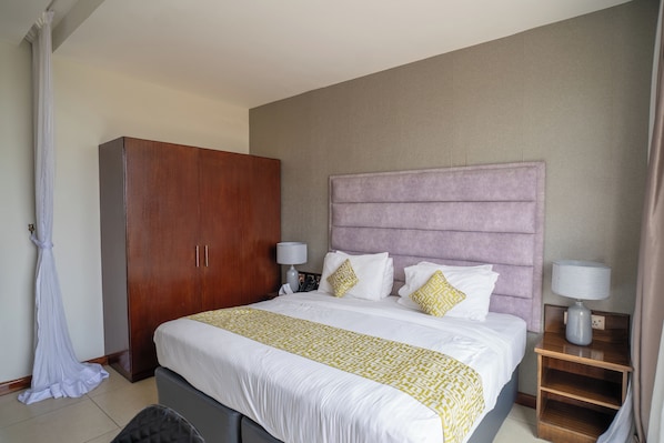 A hotel room with a large bed, a wardrobe, two bedside tables with lamps, and a curtain. - FAIRWAYS HOTEL KISUMU (Kisumu)