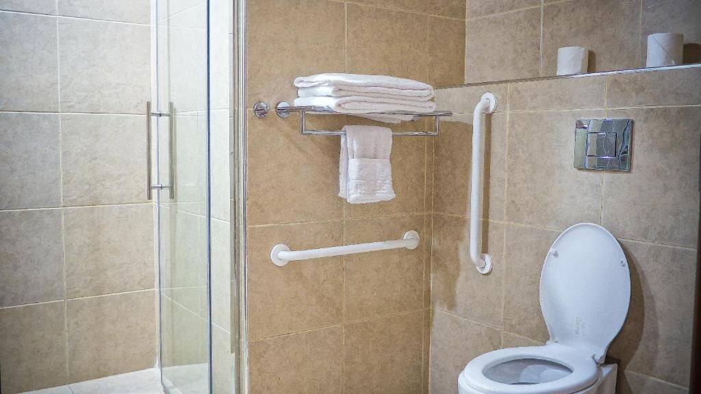 Un baño con cabina de ducha de vidrio, inodoro blanco y toallero con toallas dobladas.