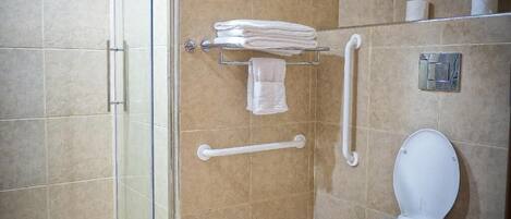 Ein Badezimmer mit Duschkabine aus Glas, einer weißen Toilette und einem Handtuchhalter mit gefalteten Handtüchern.