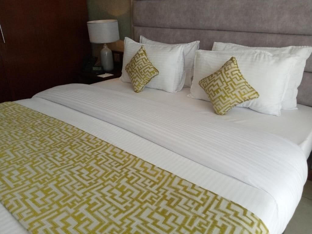 Un lit bien fait, avec du linge de lit blanc et un plaid à motifs.