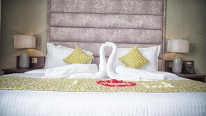 Un lit bien fait, avec du linge de lit blanc, deux oreillers à motifs géométriques et un cygne décoratif fait de serviettes.
