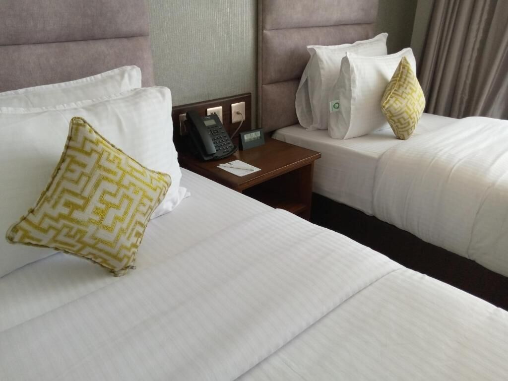 Camera d'albergo con due letti, un telefono sul comodino e un tavolino di fianco al letto.