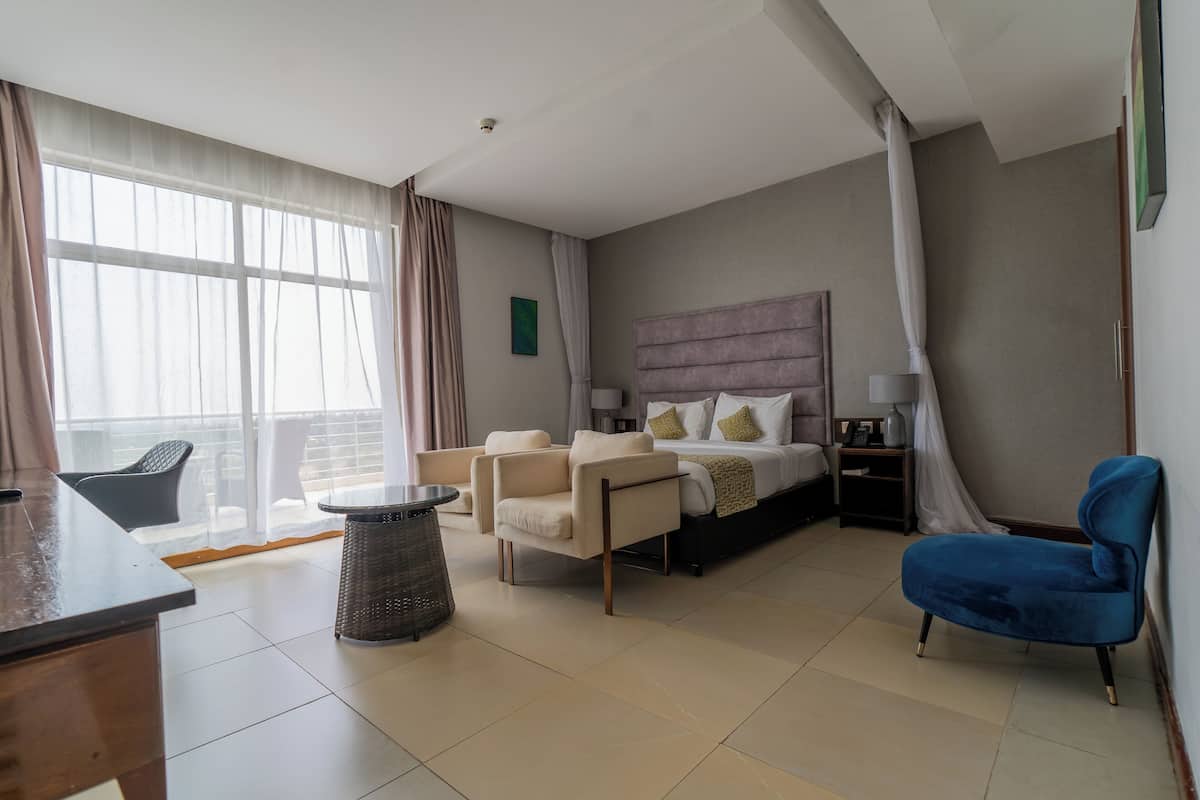 Une chambre d’hôtel moderne avec un grand lit, deux fauteuils, une petite table et un balcon avec vue.