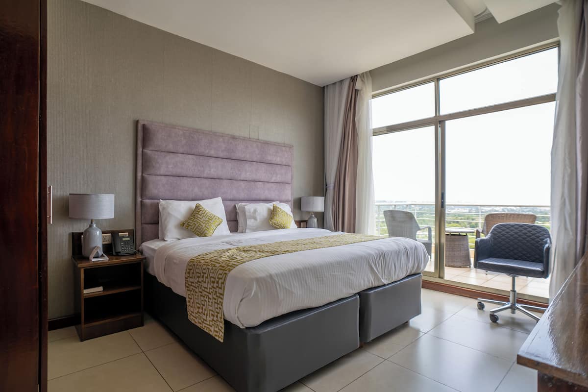 Une chambre d’hôtel moderne avec un grand lit, des lampes de chevet, une table de nuit et une vue sur l’extérieur grâce à une grande fenêtre.