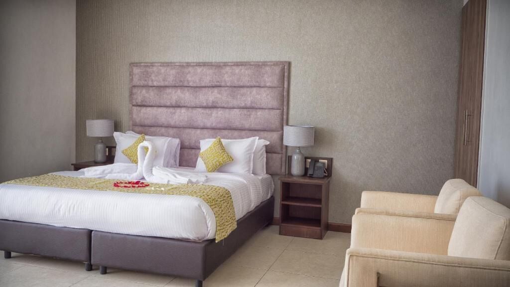 A hotel room with a large bed, two bedside tables, a chair, and a wardrobe.