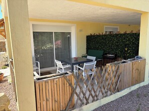 Un espace patio avec une table et des chaises, un fauteuil vert rembourré, une clôture en bois et une haie.