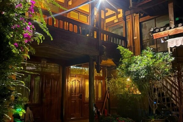 A traditional wooden building with a balcony, surrounded by lush greenery and potted plants.