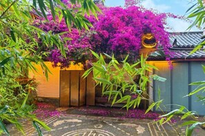 A traditional building with a tiled roof, surrounded by lush greenery and vibrant purple flowers. - Wu Suo · Li Ziyuan (Lijiang Old Town Mufu Hotel) (Lijiang)