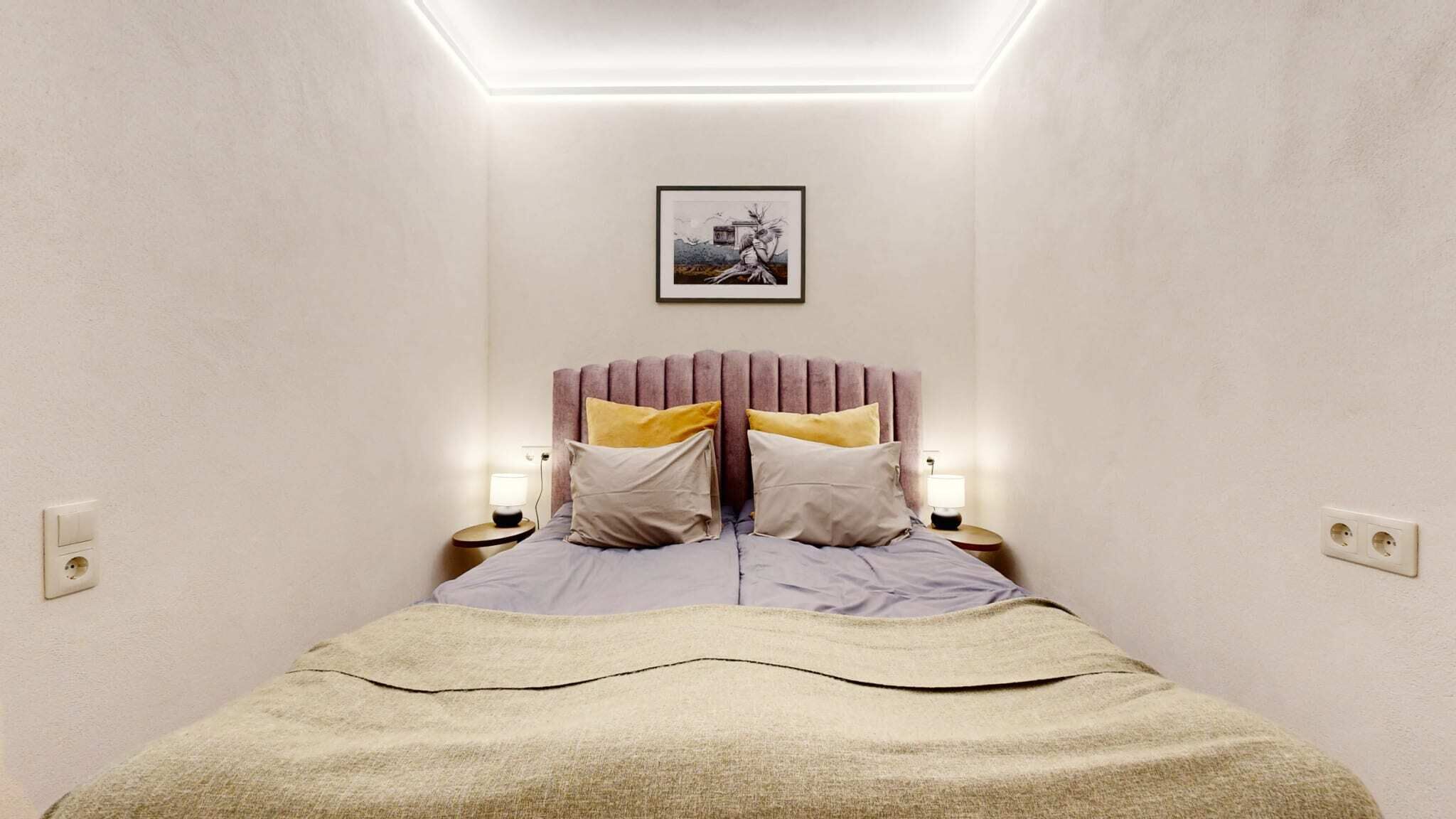 A bedroom with a bed, two bedside tables, a wall-mounted picture, and a ceiling light.