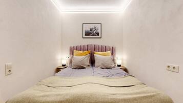 A bedroom with a bed, two bedside tables, a wall-mounted picture, and a ceiling light.