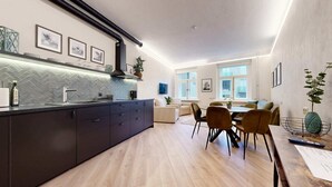 A modern kitchen with a herringbone tile backsplash, a central island with a dark countertop, and a dining area with a wooden table and chairs.