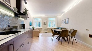 A modern kitchen with a herringbone backsplash, a dining area with a round table and chairs, and large windows providing natural light.