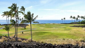 A golf course with a view of the ocean, surrounded by palm trees and volcanic rock. - Ocean Views!  8A Halii Kai (Waikoloa Beach Resort)