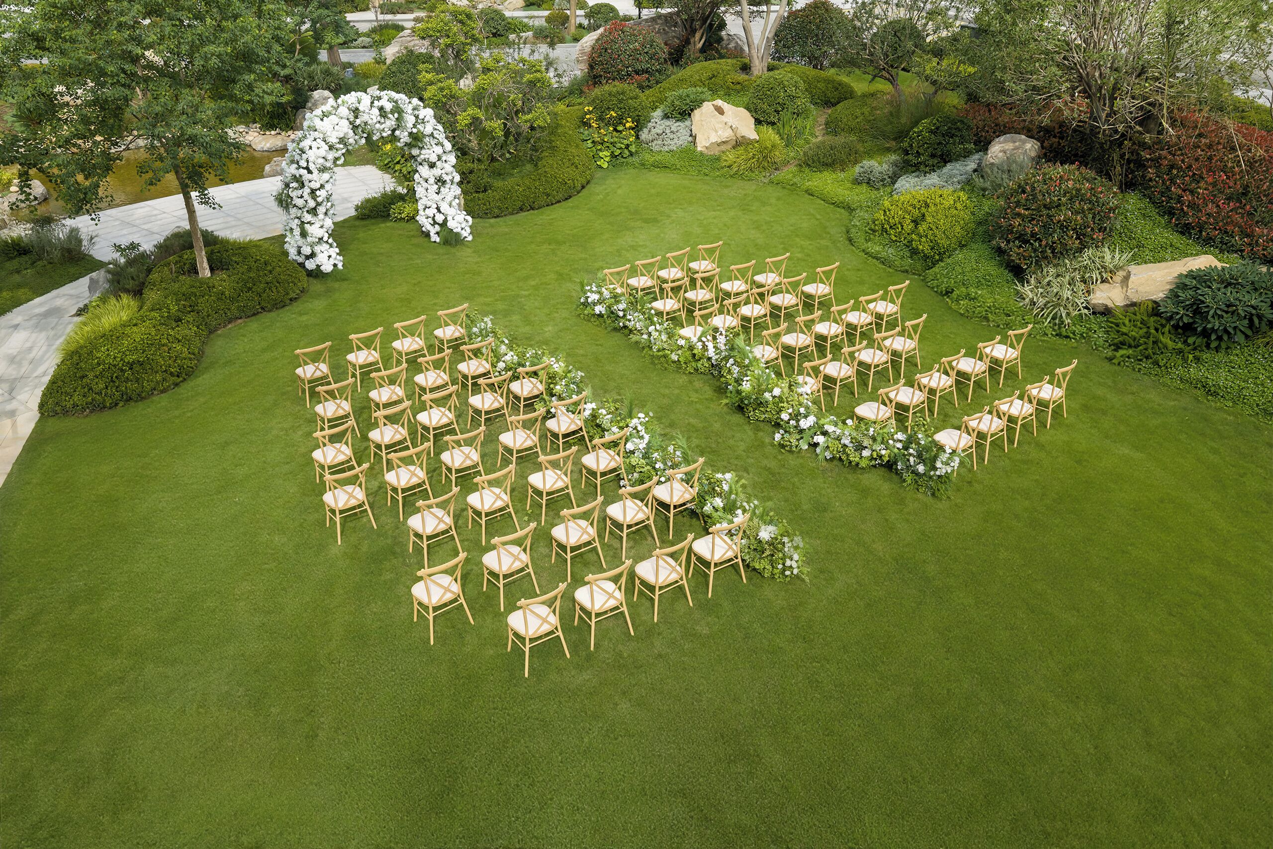 Eine Hochzeitslocation im Freien mit Rasenfläche, Holzstühlen und einem Blumengestall.