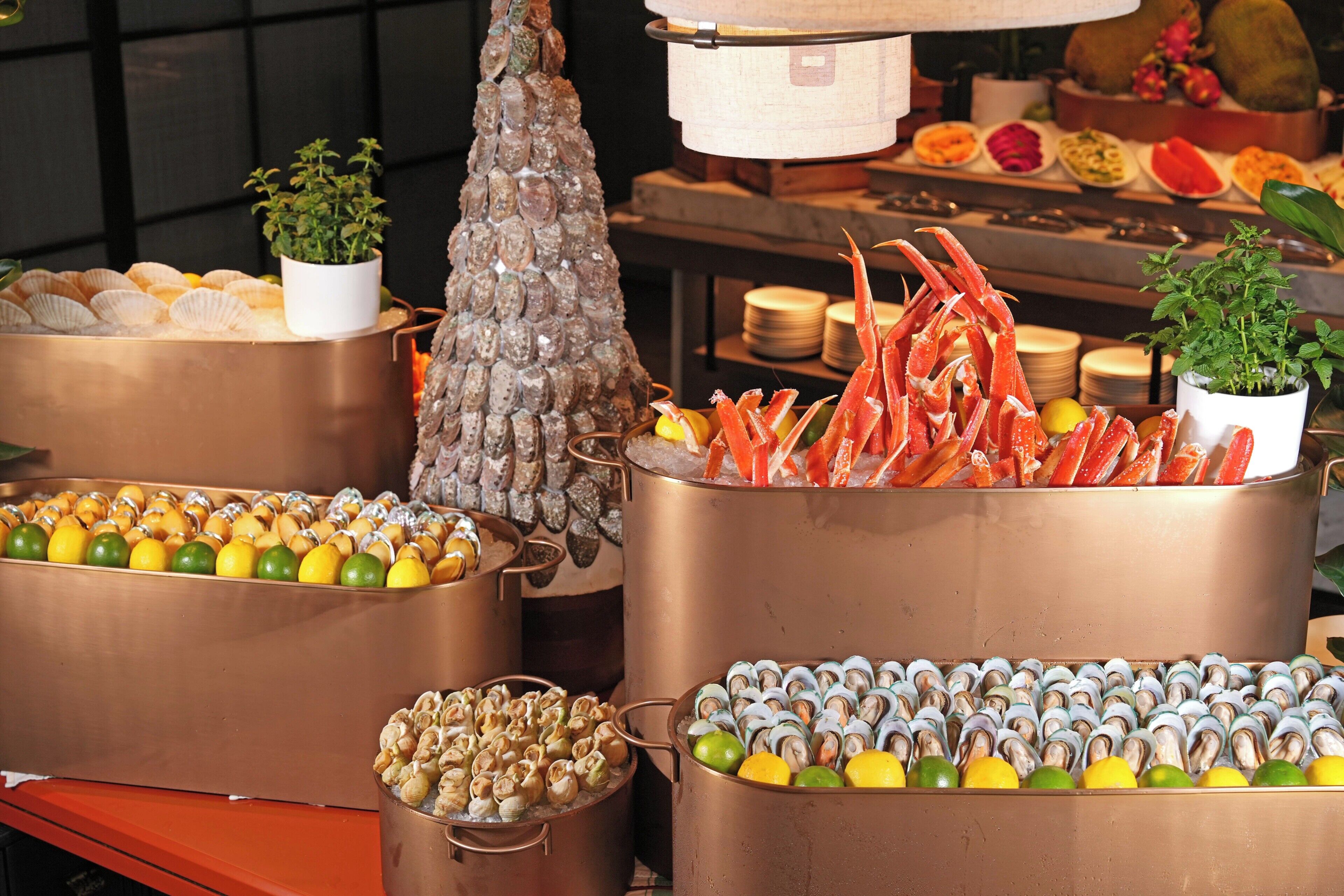 Exhibición de mariscos con diversos tipos de mariscos y crustáceos, como ostras, almejas y cangrejos, dispuestos en recipientes de cobre.