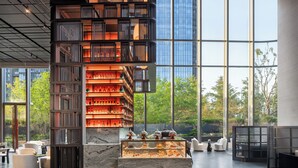 Un interior moderno con una vitrina central, una estantería escalonada y una zona de estar con vistas al exterior.