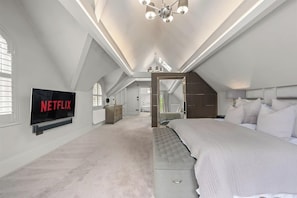A spacious bedroom with a large bed, a TV mounted on the wall, and a staircase leading to an upper level.