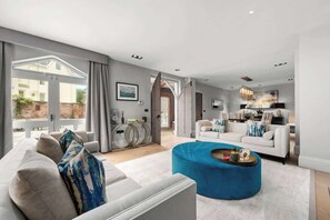A modern living room with a sofa, a blue ottoman, and a dining area with a table and chairs.