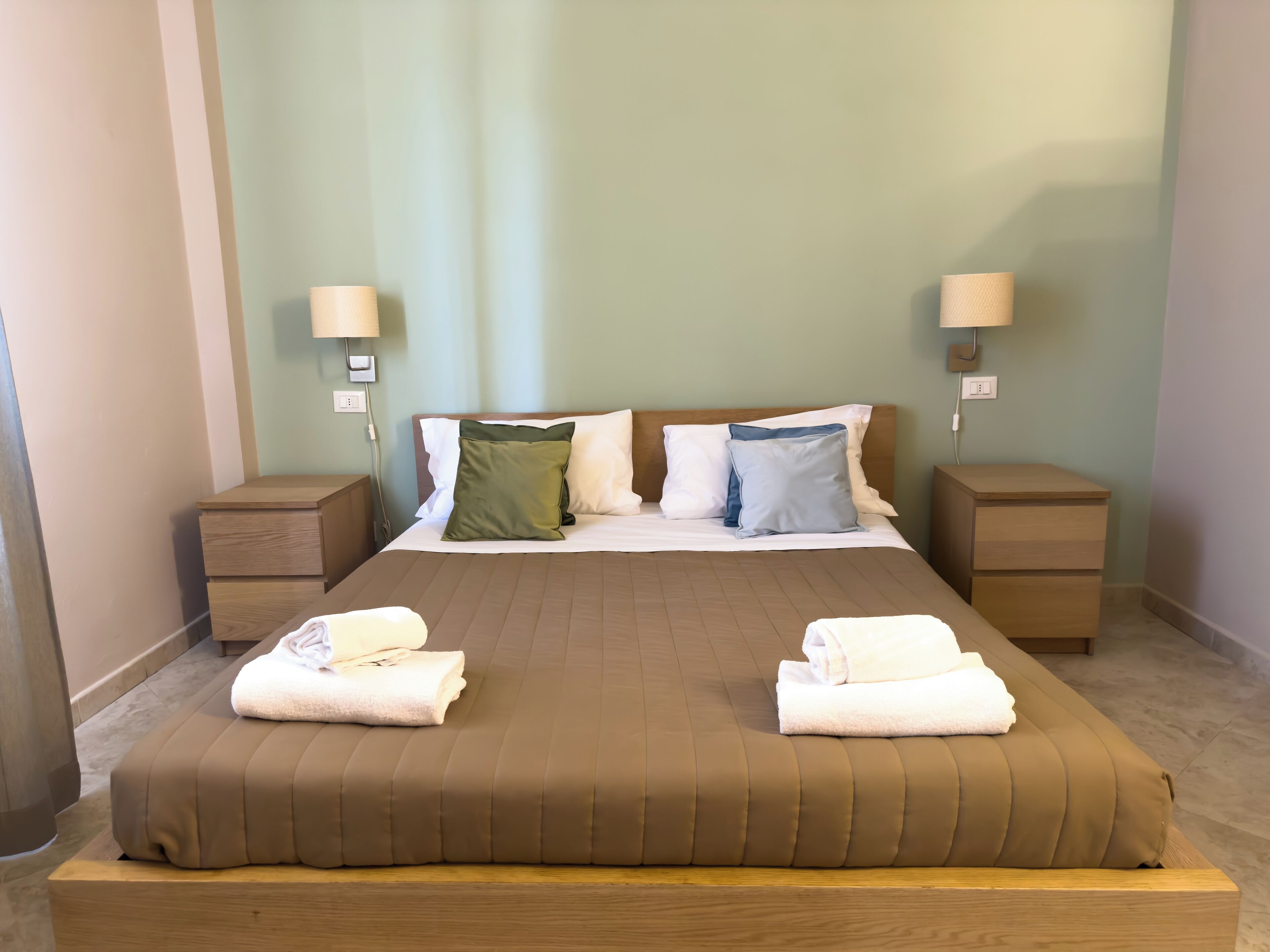 A neatly made bed with a brown cover, two bedside tables with lamps, and a green wall.