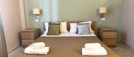 A neatly made bed with a brown cover, two bedside tables with lamps, and a green wall.
