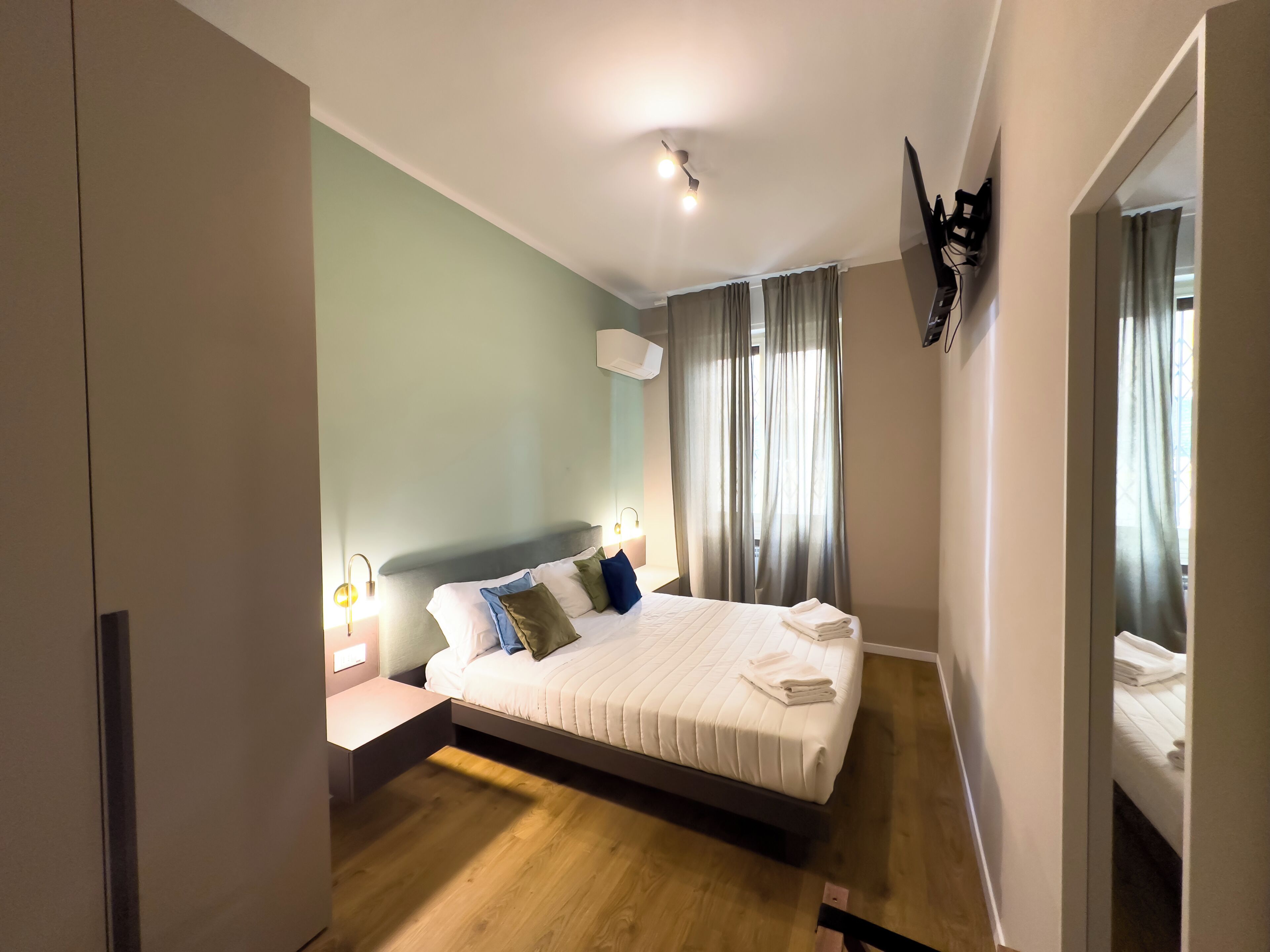 A modern hotel room with a large bed, a bedside table, a mirror, and a ceiling light.