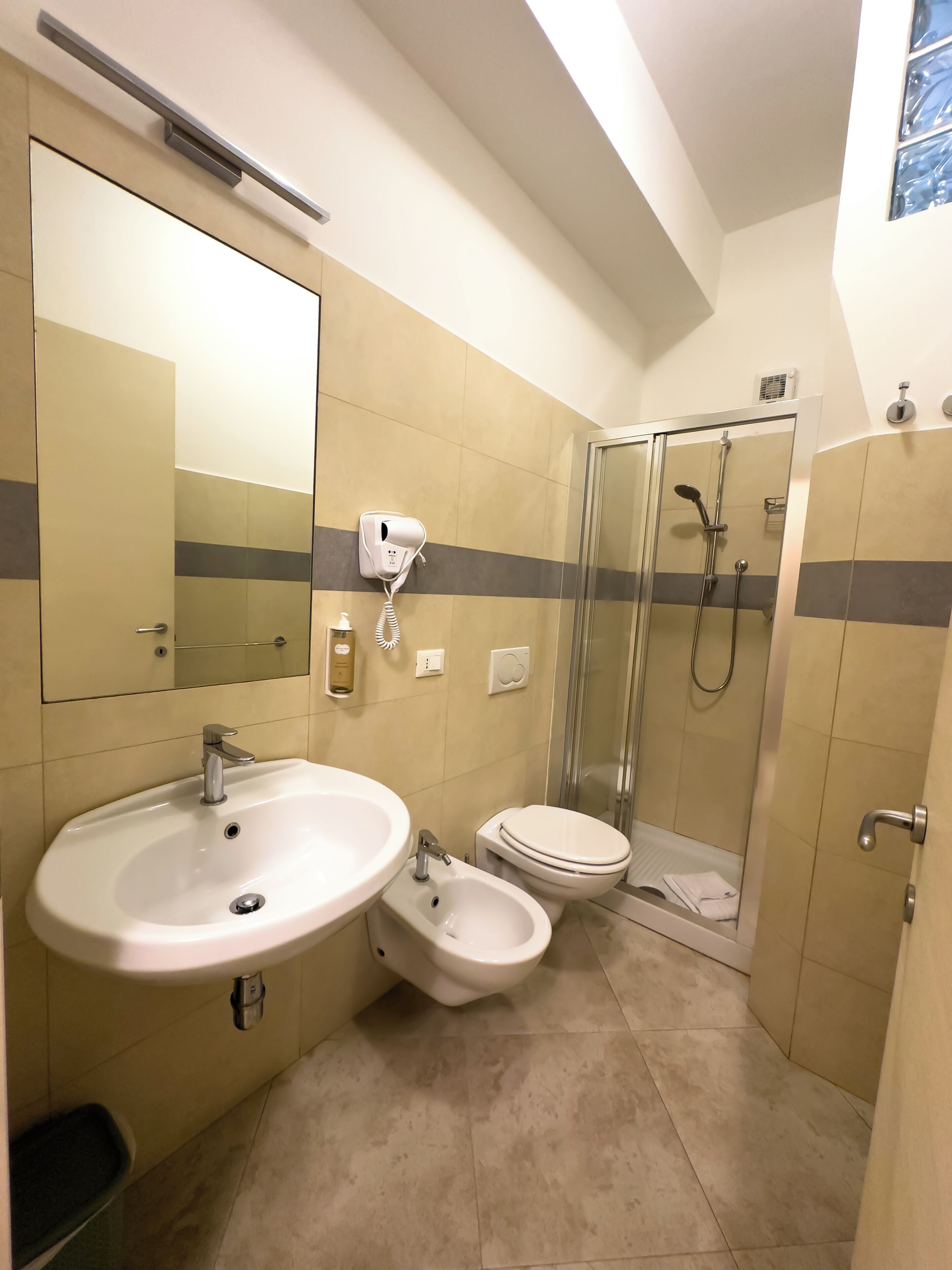 A bathroom with a large mirror, two sinks, a toilet, and a glass-enclosed shower.