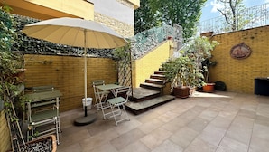 A patio with a table and chairs, a large umbrella, potted plants, and a staircase leading to an upper level. - SWEET HOME COSSERIA (Florence)