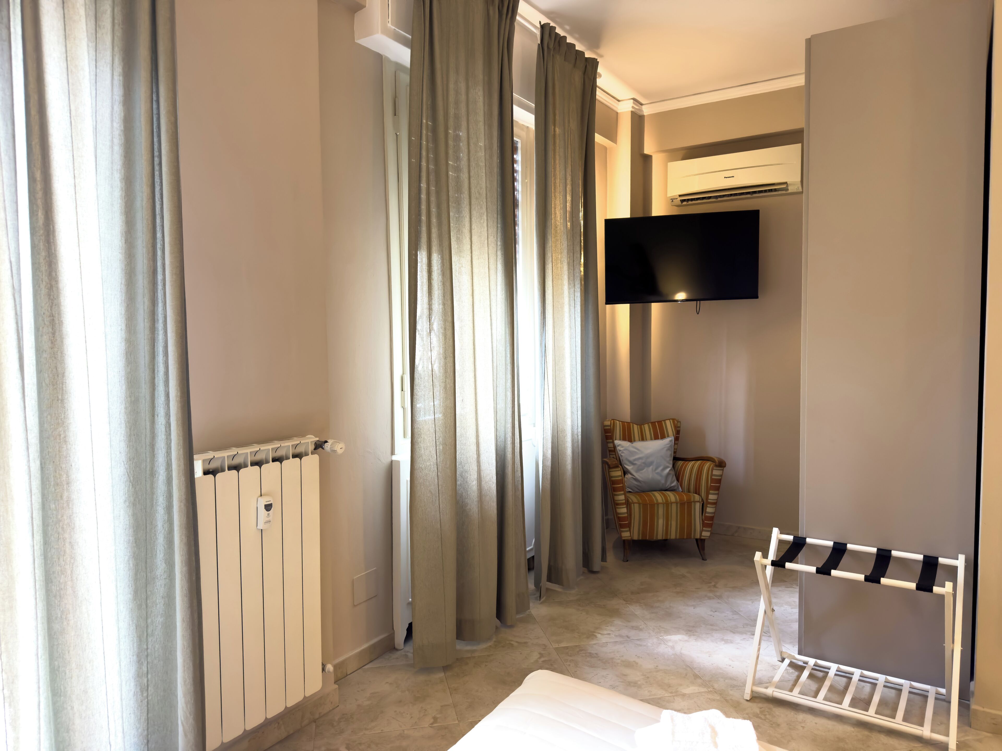 Hotellihuone, jossa on sänky, tuoli, seinälle asennettu televisio ja patteri.