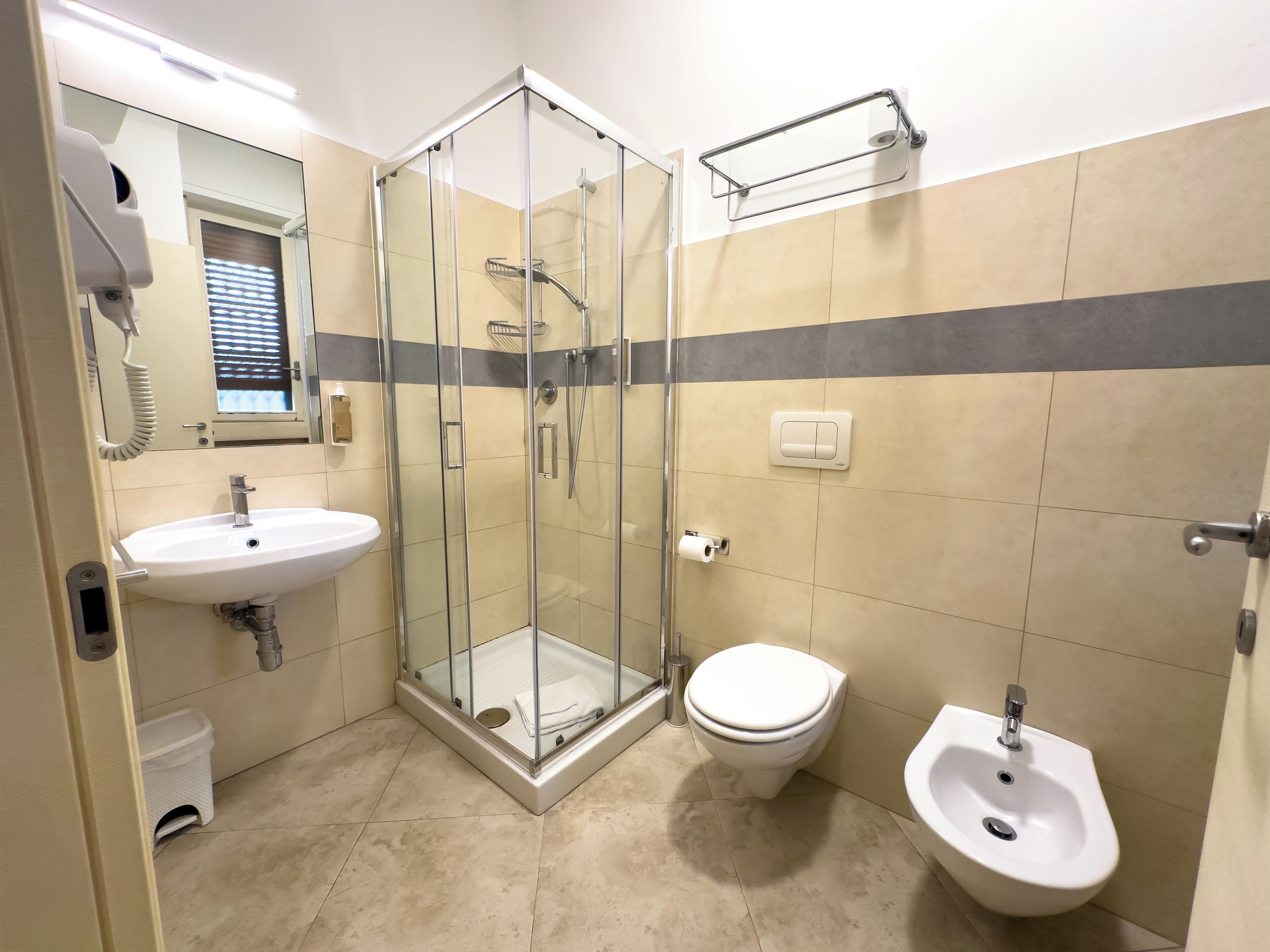 A bathroom with a glass-enclosed shower, a sink, a toilet, and a bidet.