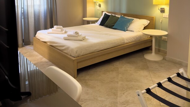 A hotel room with a bed, bedside tables, a desk, a chair, an air conditioning unit, and a TV. - SWEET HOME COSSERIA (Florence)
