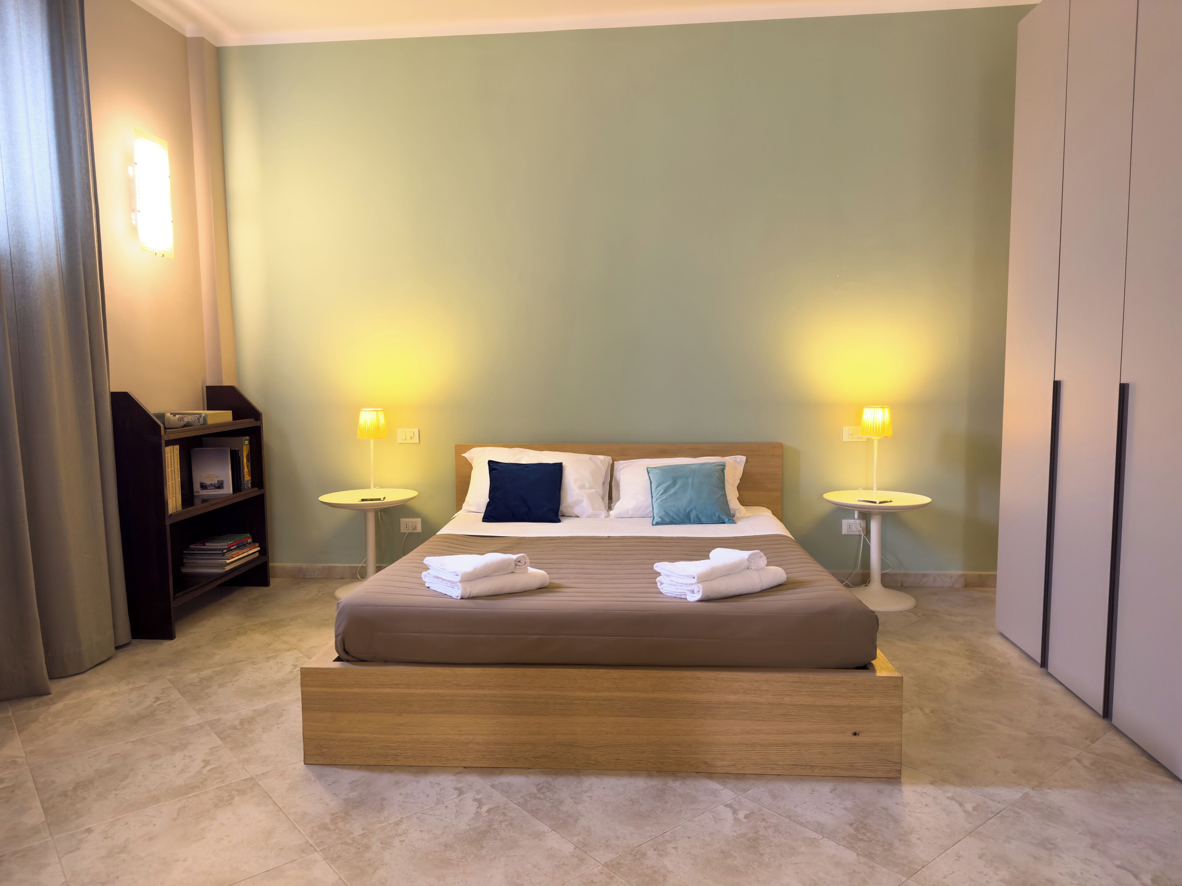 A hotel room with a bed, two bedside tables, a bookshelf, and a wardrobe.