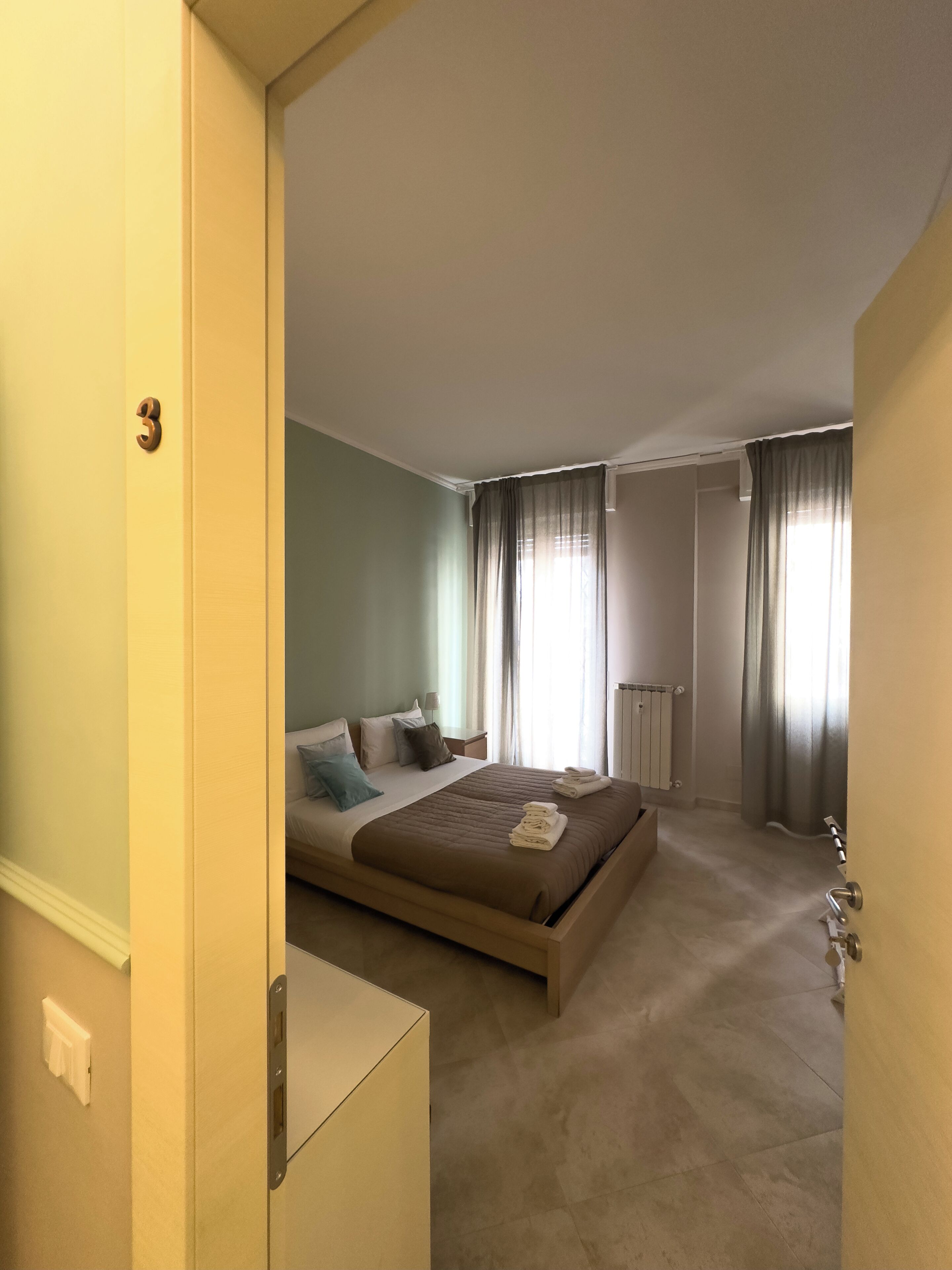 A bedroom with a bed, bedside tables, a radiator, and curtains.