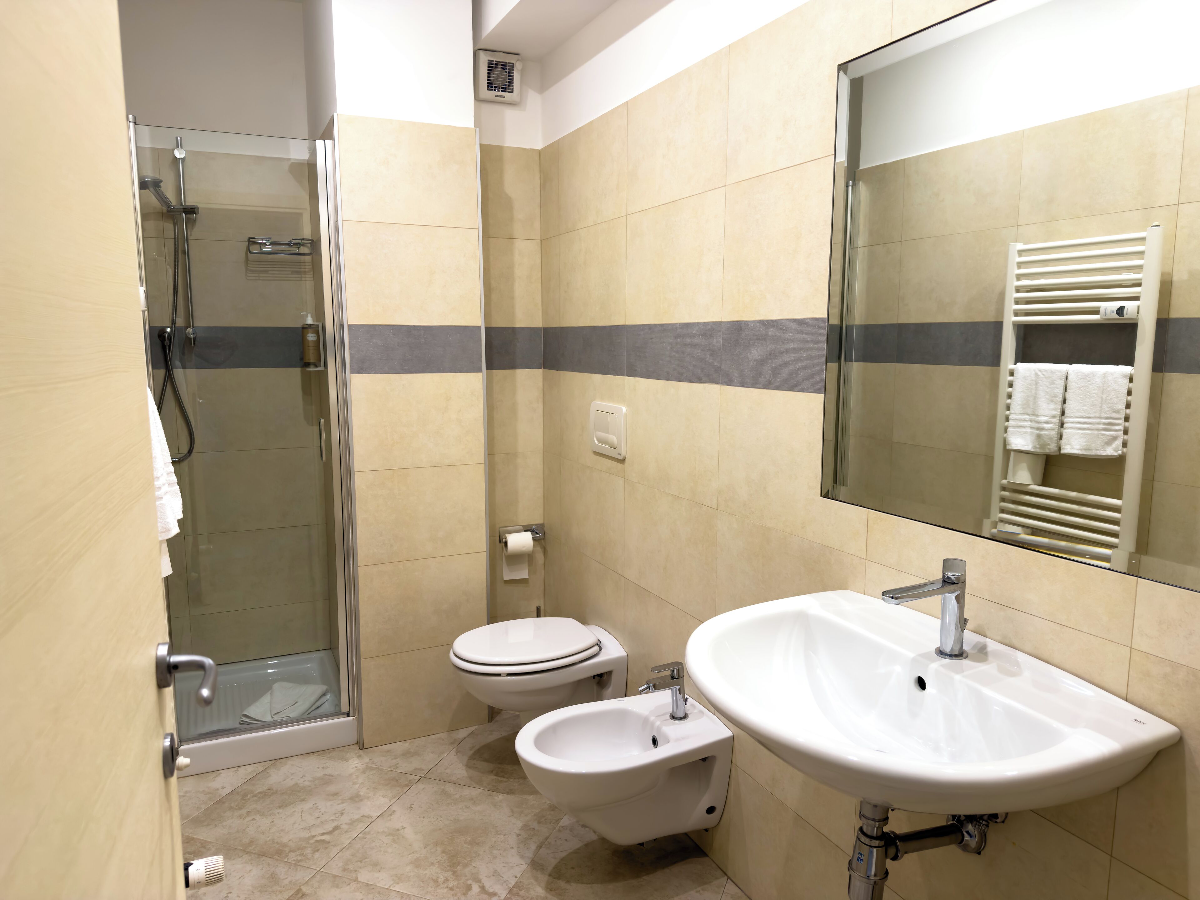 A modern bathroom with a glass shower enclosure, a toilet, a bidet, and a sink with a mirror.