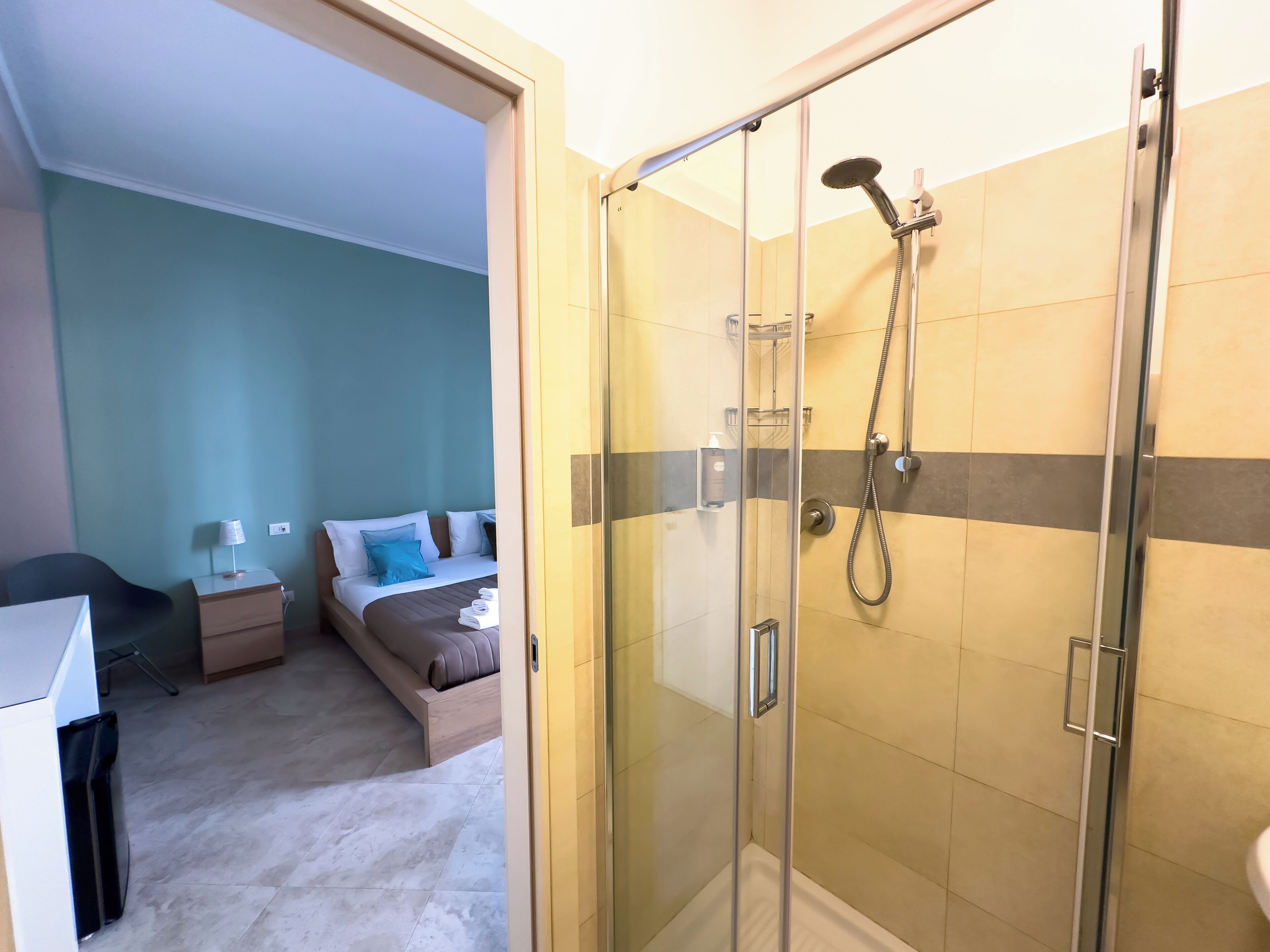Une chambre d’hôtel avec une douche en verre, un lit avec des oreillers bleus, un bureau et une chaise.