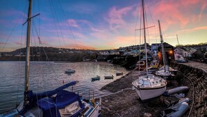 A harbor with boats docked, a rocky waterfront, and buildings in the background. - Sailhouse Loft, New Quay (New Quay)