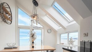 A modern kitchen with skylights, a wooden dining table, and a view of the sea.