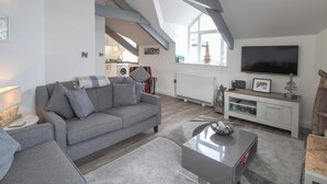 A modern living room with a grey sofa, a coffee table, and a TV mounted on the wall. - Sailhouse Loft, New Quay (New Quay)