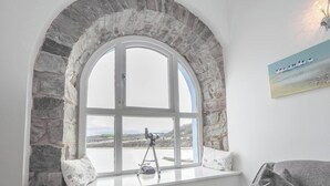 A room with a stone arch window, a telescope on a tripod, and a painting on the wall. - Sailhouse Loft, New Quay (New Quay)