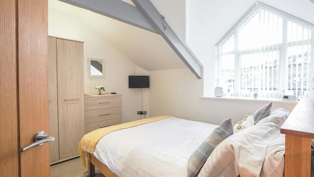 A bedroom with a bed, a dresser, a TV, and a window with a view of buildings.